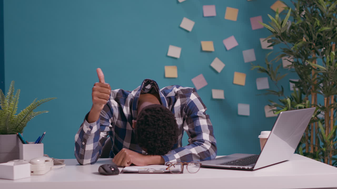 Overworked man putting head on desk and showing okay sign