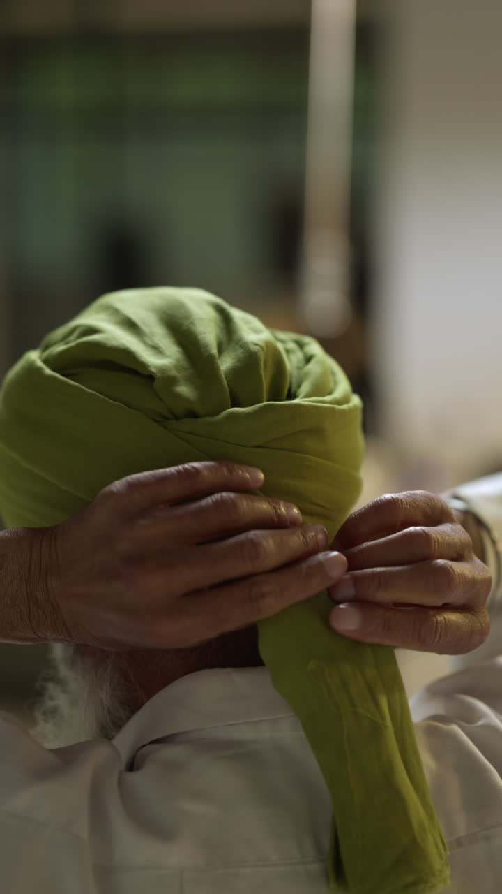 una toma de video vertical de un anciano sikh con barba atando tela para un turbante mirándose en el espejo desde atrás