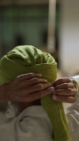 vertical video shot of senior sikh man with beard tying fabric for turban looking in mirror from behind