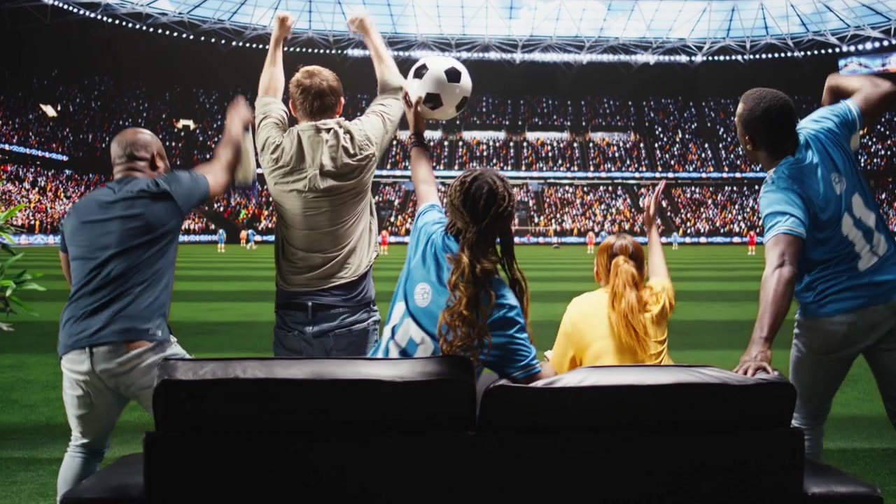 Aficionados de fútbol celebran un gol en casa, viendo el partido en una transmisión interactiva por televisión.
