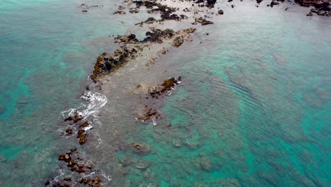 aerial view above white wash waves on lava rocks and reef in clear turquoise ocean in hawaii