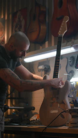 woodworking specialist fixes the neck of the guitar to the guitar body professional male craftsman fixes the neck of the guitar to the guitar body woodworking specialist carpenter makes wooden musical instrument in modern workshop handcraft and small business concept