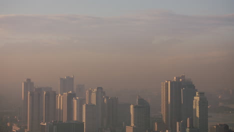 Tiro-Inclinado-Hacia-Abajo-En-Cámara-Lenta-De-Las-Torres-De-La-Bahía-De-Manila-Siendo-Golpeadas-Por-La-Luz,-Durante-Un-Hermoso-Amanecer