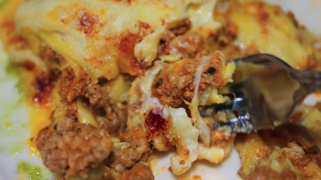 Close up of a fork picking up lasagna from a white plate