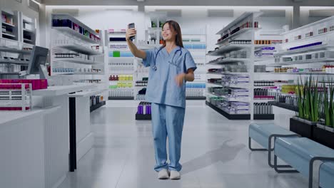 cuerpo lleno de médico asiático con estetoscopio agitando la mano y teniendo una llamada de video en el teléfono inteligente mientras estaba de pie en la farmacia