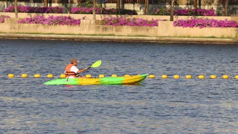 person kayaking past colorful flowers on river