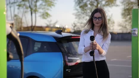 woman stands with phone near her electric car and waits when vehicle will charged
