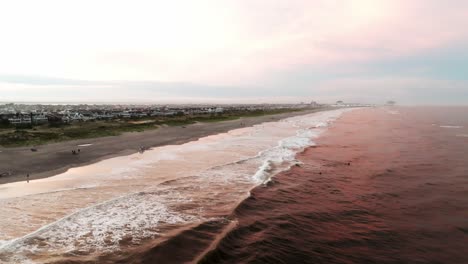 Hermosa-Puesta-De-Sol-En-La-Playa-Sobre-Las-Olas-Rompiendo-Con-Vistas-A-Las-Casas-De-Vacaciones