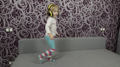 Little-happy-child-jumping-and-dancing-on-sofa-and-listening-music-in-headphones