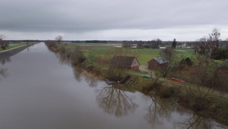 Luftaufnahme-Von-Hochwasser-Im-Frühling,-Überschwemmung-Des-Barta-Flusses,-Braunes-Und-Schlammiges-Wasser,-Bewölkter-Tag,-Abgelegenes-Haus-Am-Ufer-Des-Flusses,-Weit-Aufsteigende-Drohnenaufnahme,-Die-Sich-Rückwärts-Bewegt