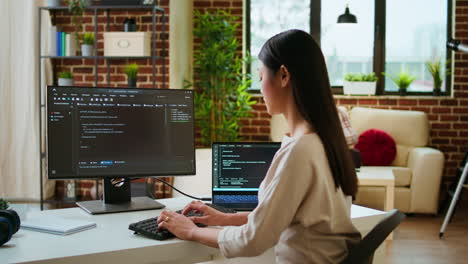 asian programmer seen typing code for a user interface design on dual monitors