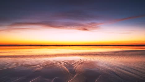 Lebhafter-Sonnenuntergang,-Der-Sich-Im-Nassen-Sand-Spiegelt,-Und-Am-Ende-Des-Zeitraffers-Schleichen-Sich-Schatten-Ein