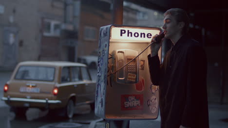 young man speaking on pay phone on rainy urban street