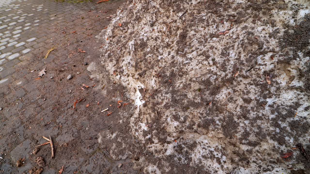 Schmutzige Schneewehe auf einem Bürgersteig in der Stadt nach dem Winter, bedeckt mit Streusplitt und Salz, während tauender Schneematsch zu schlammigem Abfluss schmilzt – Konzept für saisonale Stadtreinigung und Sicherheit