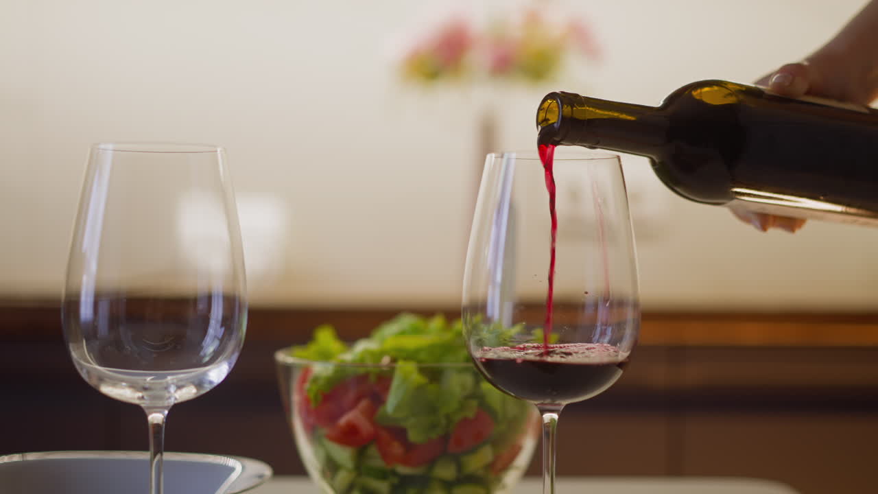 Person pours red wine into glass preparing romantic dinner