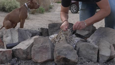 hands of man trying to start campfire with flint and steel, dog and car in background, slow motion