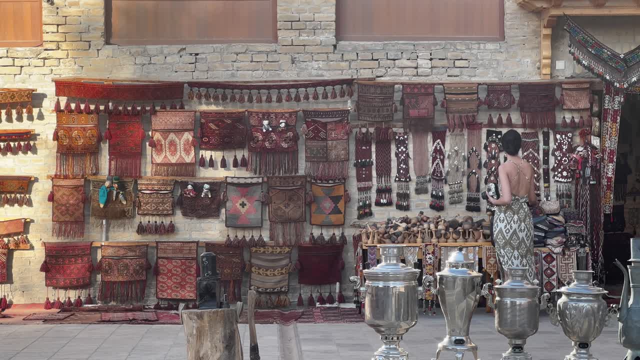 Traditional Craftsmanship of Uzbekistan: 4K Static Shot of a Young Female Photographer Examining Traditional Carpets, Woodcraft and other Handmade Central Asian Artifacts in Bukhara Old Town