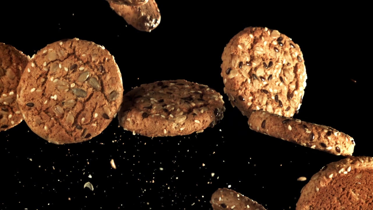 Biscotti d'avena con semi in caduta al rallentatore su sfondo nero