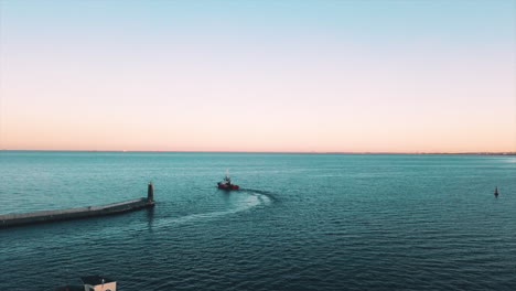 Drone-Volando-Hacia-Un-Barco-De-Pesca-Navegando-Fuera-De-La-Bahía-Al-Atardecer