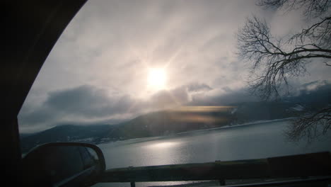 Vista-Desde-La-Ventana-Lateral-Del-Coche-En-El-Lago-Y-Las-Montañas-Retroiluminadas-Por-El-Sol-En-Cámara-Lenta