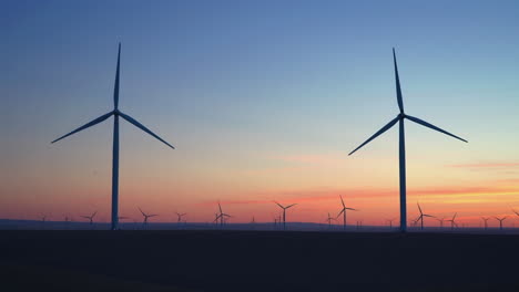 silhouetted wind turbines at work against vivid sunset sky. wide
