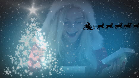 animation of santa claus in sleigh with reindeer over christmas tree and caucasian woman with gift