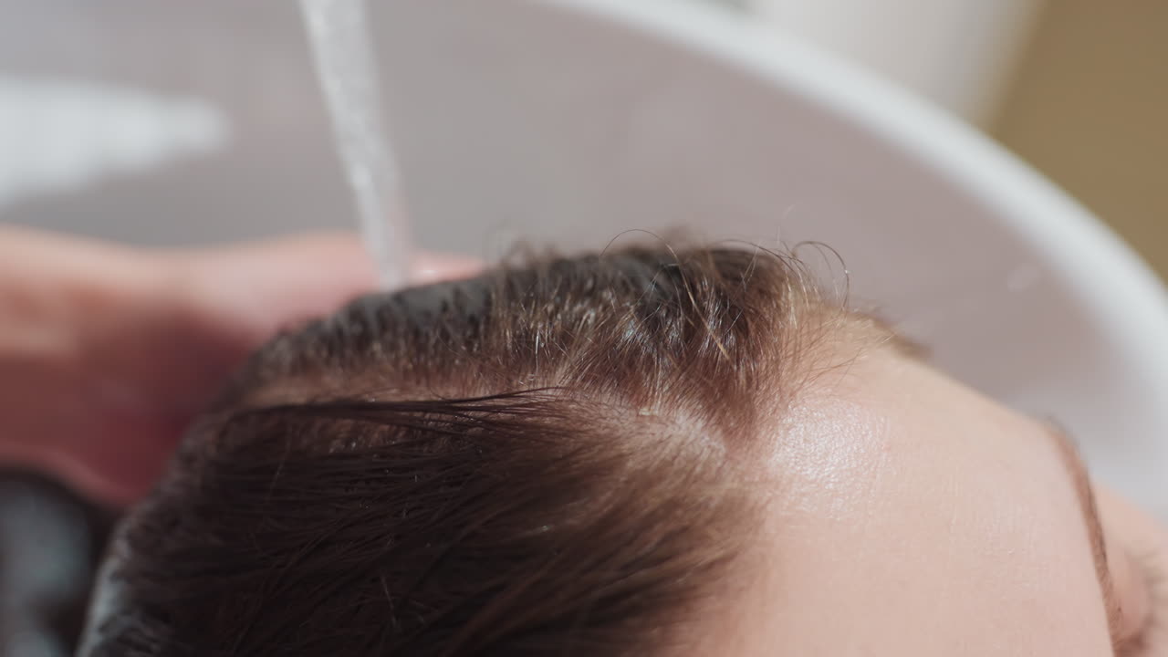 전문적인 두피 및 모발 세정 과정, 꾸준한 물줄기가 꼼꼼하게 모근과 헤어라인을 정화하며, 숙련된 손길로 두피와 모발을 부드럽게 세정하는 섬세한 장면을 담은 클로즈업 샷