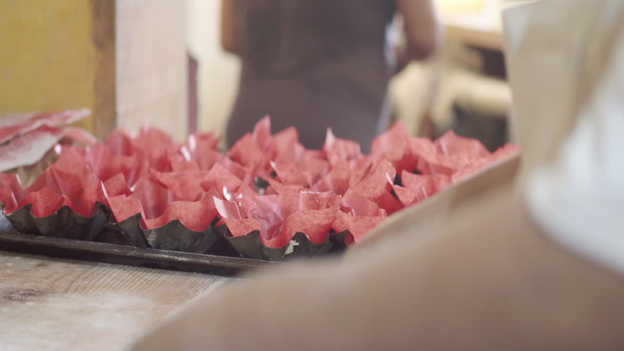 A pastry chef places red liners into a baking tray, preparing to bake muffins or cupcakes