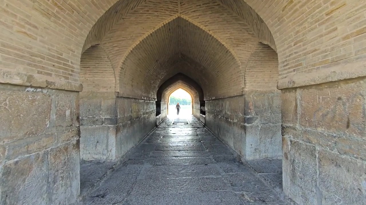 Persona che cammina attraverso un antico arco in pietra di un ponte storico.
