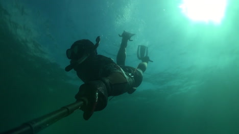 Hombre-Pato-Se-Sumerge-Bajo-El-Agua-Usando-Un-Traje-De-Neopreno-Completo-En-Agua-Fría-Y-Sosteniendo-Un-Palo-Selfie-Con-Go-Pro