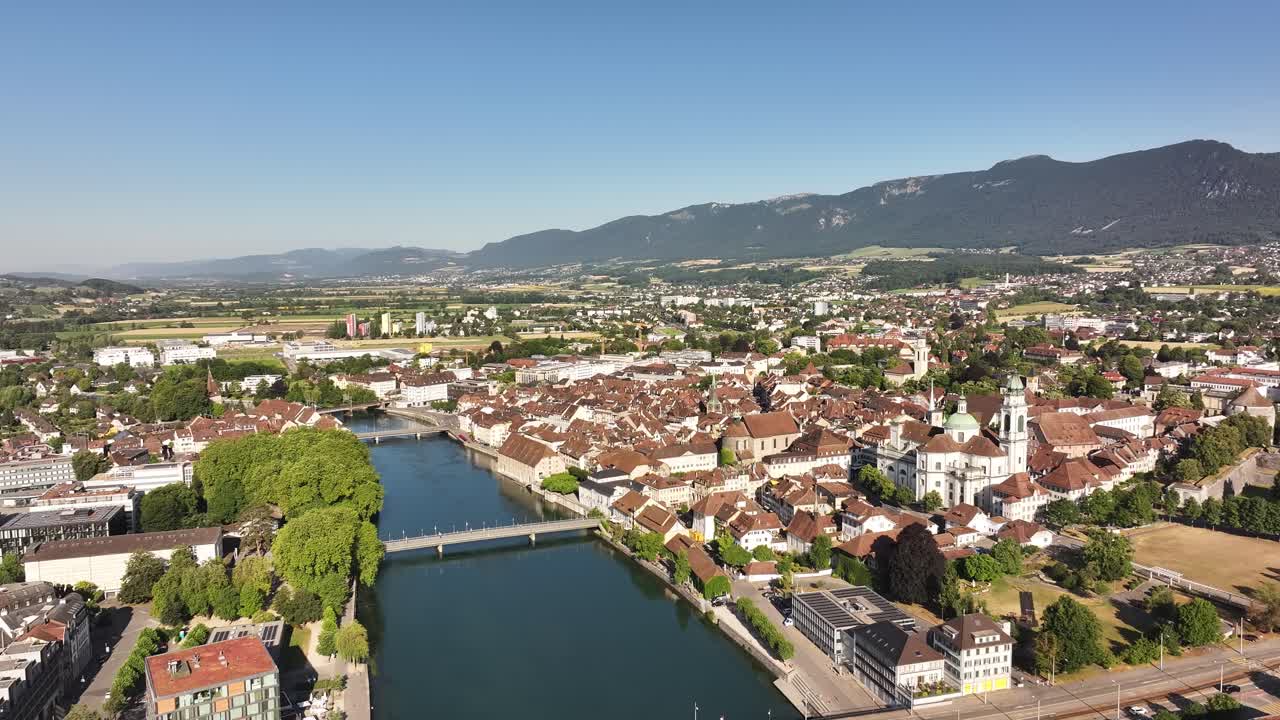 Aerial view of the city of Olten, Switzerland, with the Aare River flowing through its center. The historic cityscape is framed by green hills under a bright, the Swiss canton of Solothurn