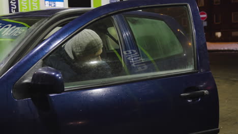 white man parks dark blue car at gas station walks around to fill petrol