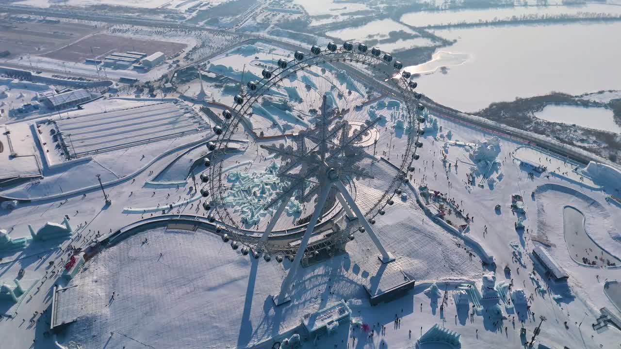 Drone shot of the famous Snowflake Ferris Wheel at the Harbin Ice Festival 2025. The massive frozen-themed attraction stands amidst intricate ice sculptures. China