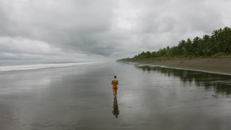 aerial follows a young man that walks on an empty beach, colombia
