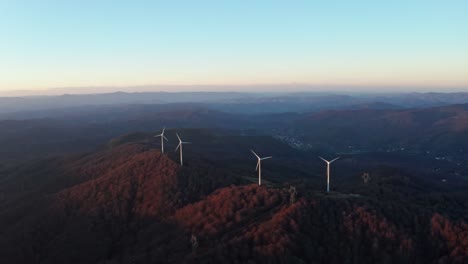wind turbines crown the forested ridges at twilight with distant mountains in a serene aerial view
