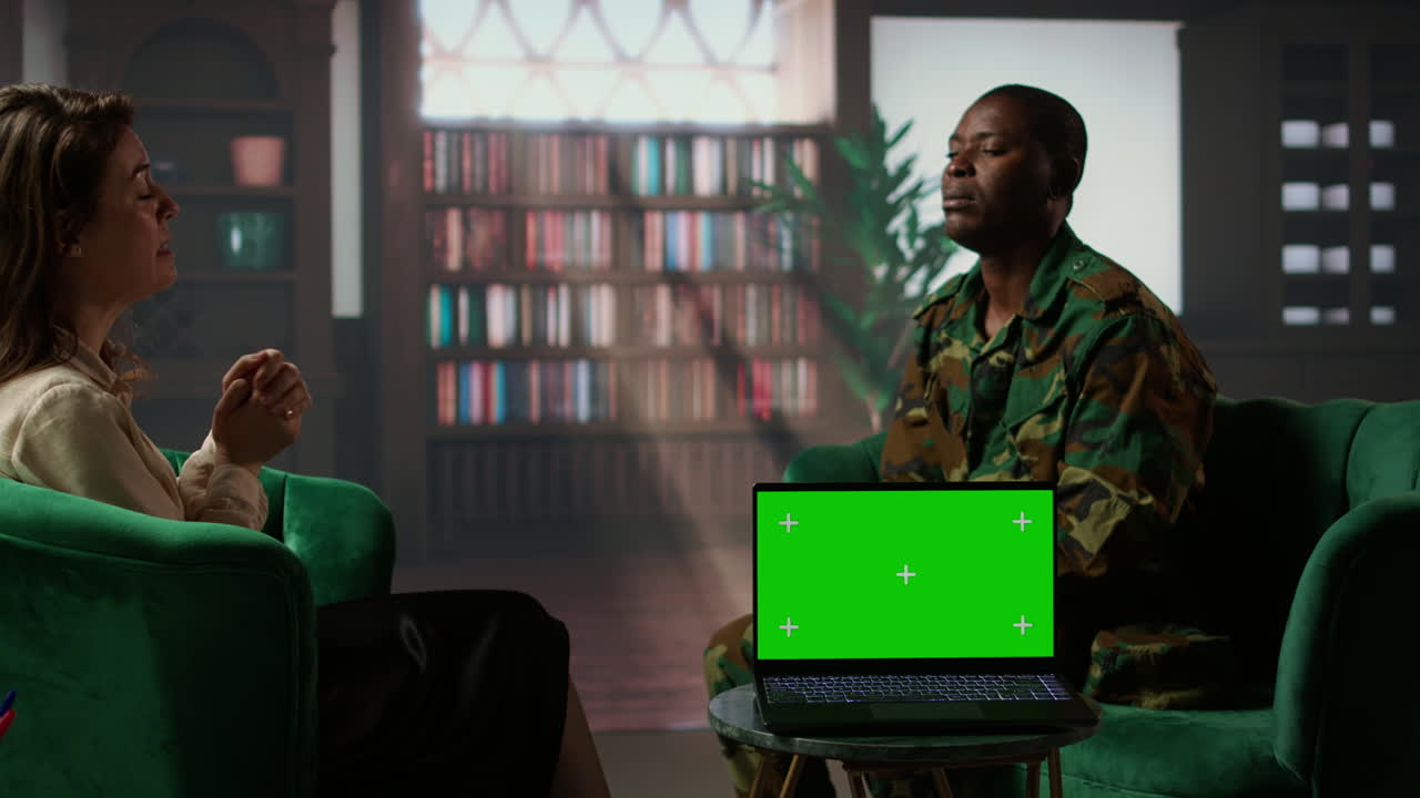 Military personnel discuss with a therapist next to chroma key screen