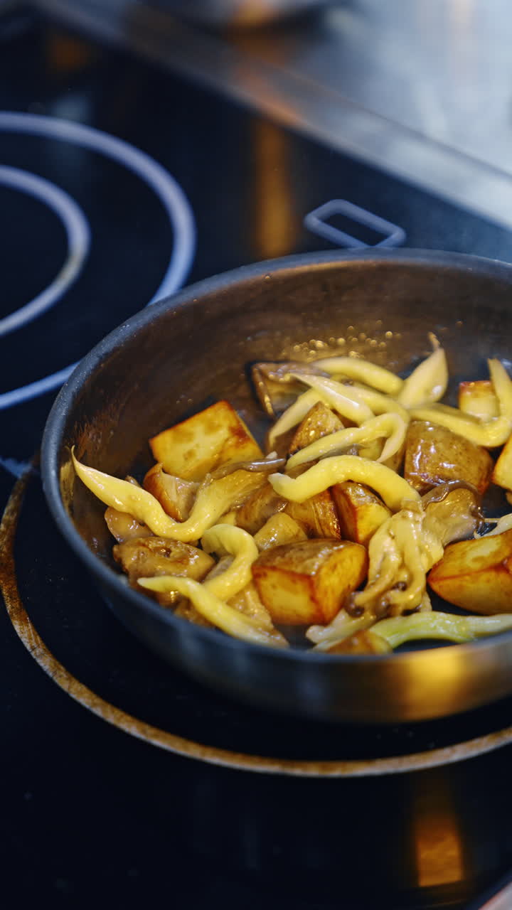 Potatoes and mushrooms are fried on the frying pan. Cook shakes the pan to stir the dish. Vertical video.