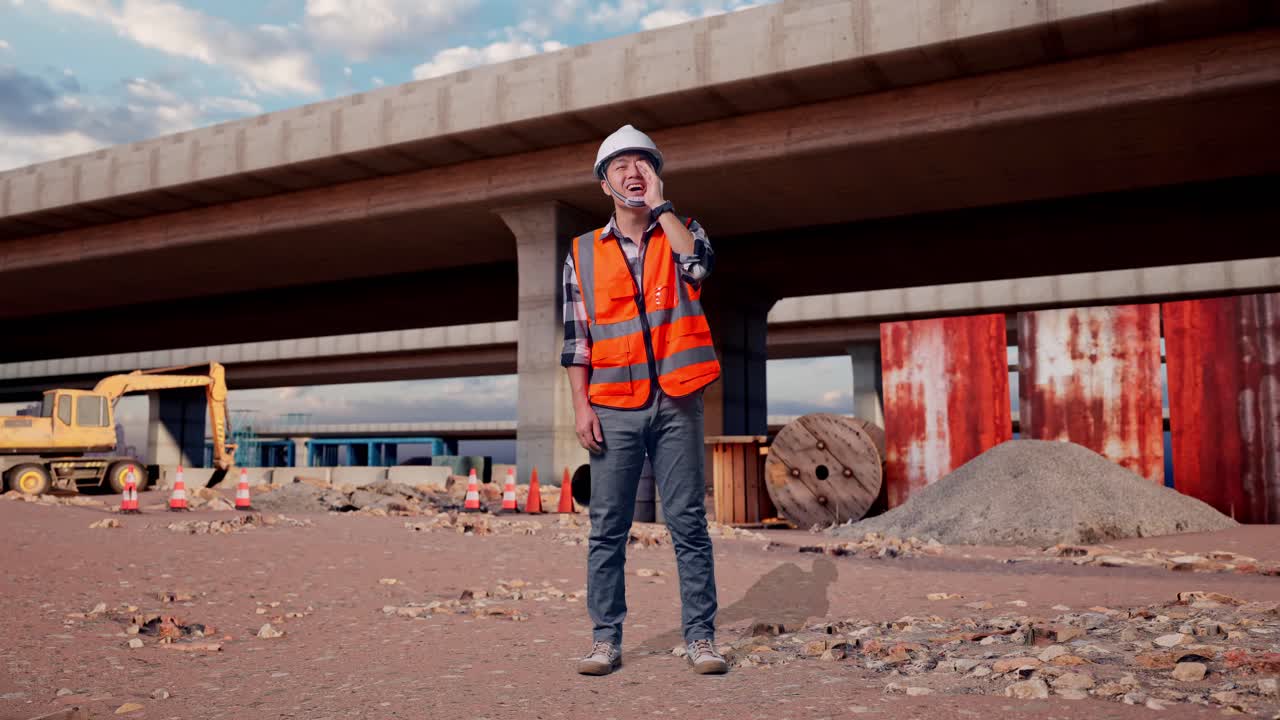 Full Body Of Asian Male Engineer With Safety Helmet Yelling With Hand Over Mouth While Standing At The Site of Highway Construction