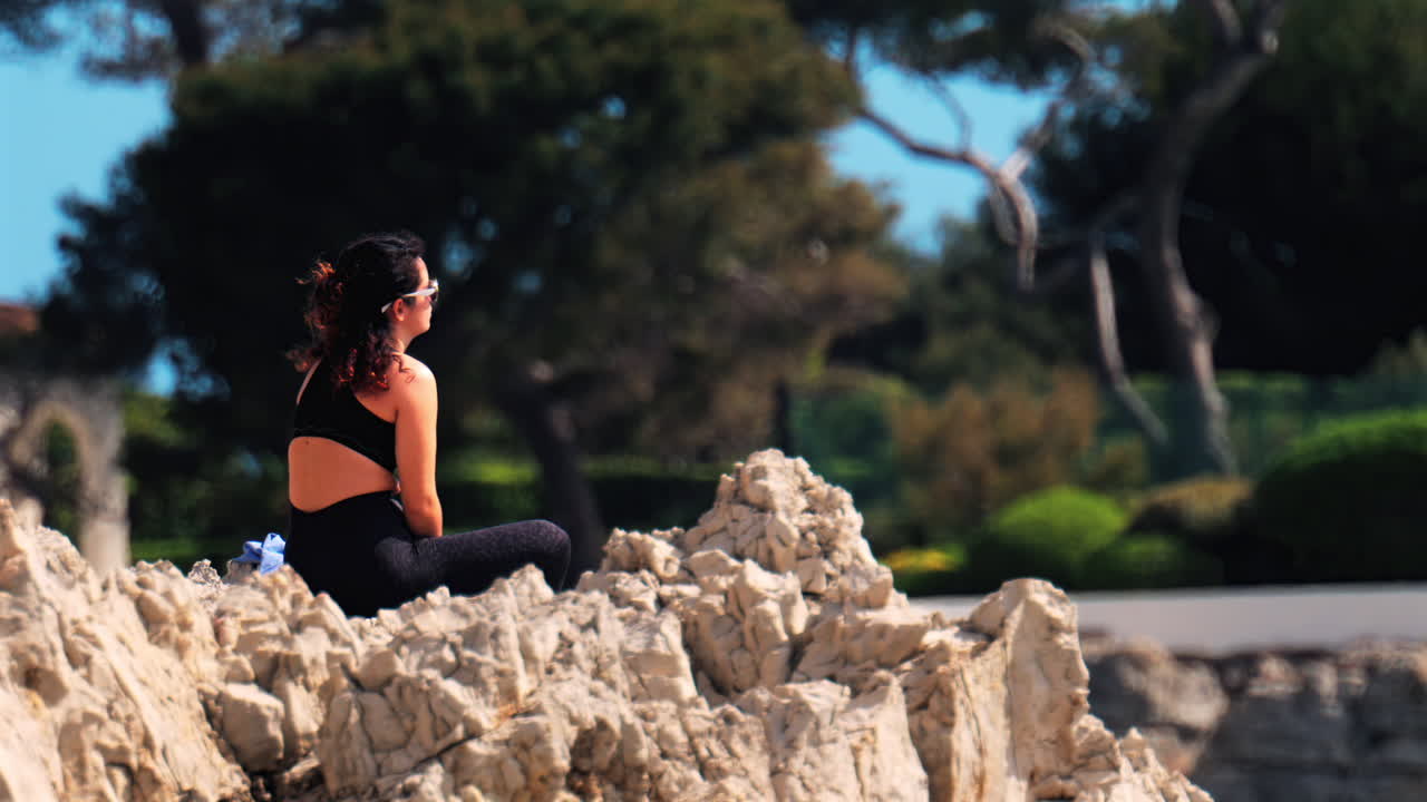 Woman wearing a black sportswear set resting on the rocks with trees on the background