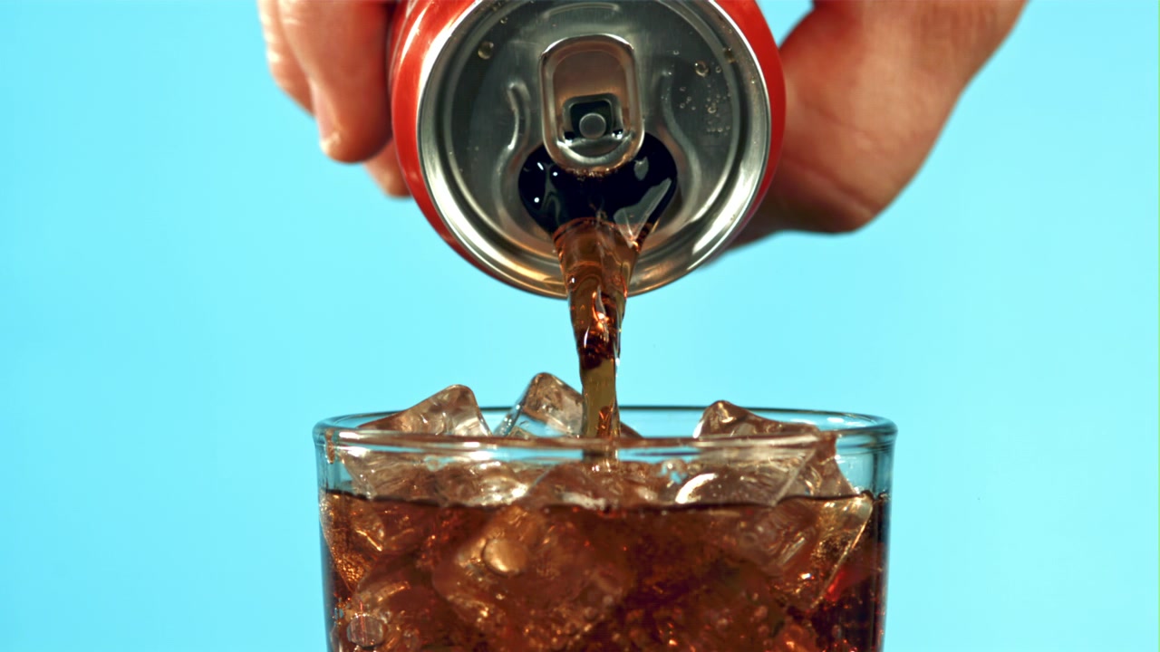 Cola rinfrescante versata da una lattina rossa in un bicchiere con cubetti di ghiaccio