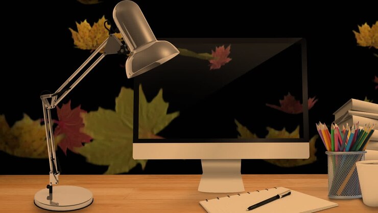 Desktop computer and office equipment on a table against autumn maples leaves falling in background