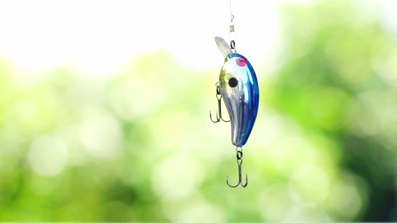 A shiny fish-shaped fishing lure is attached to a fishing line and dangled swayingly