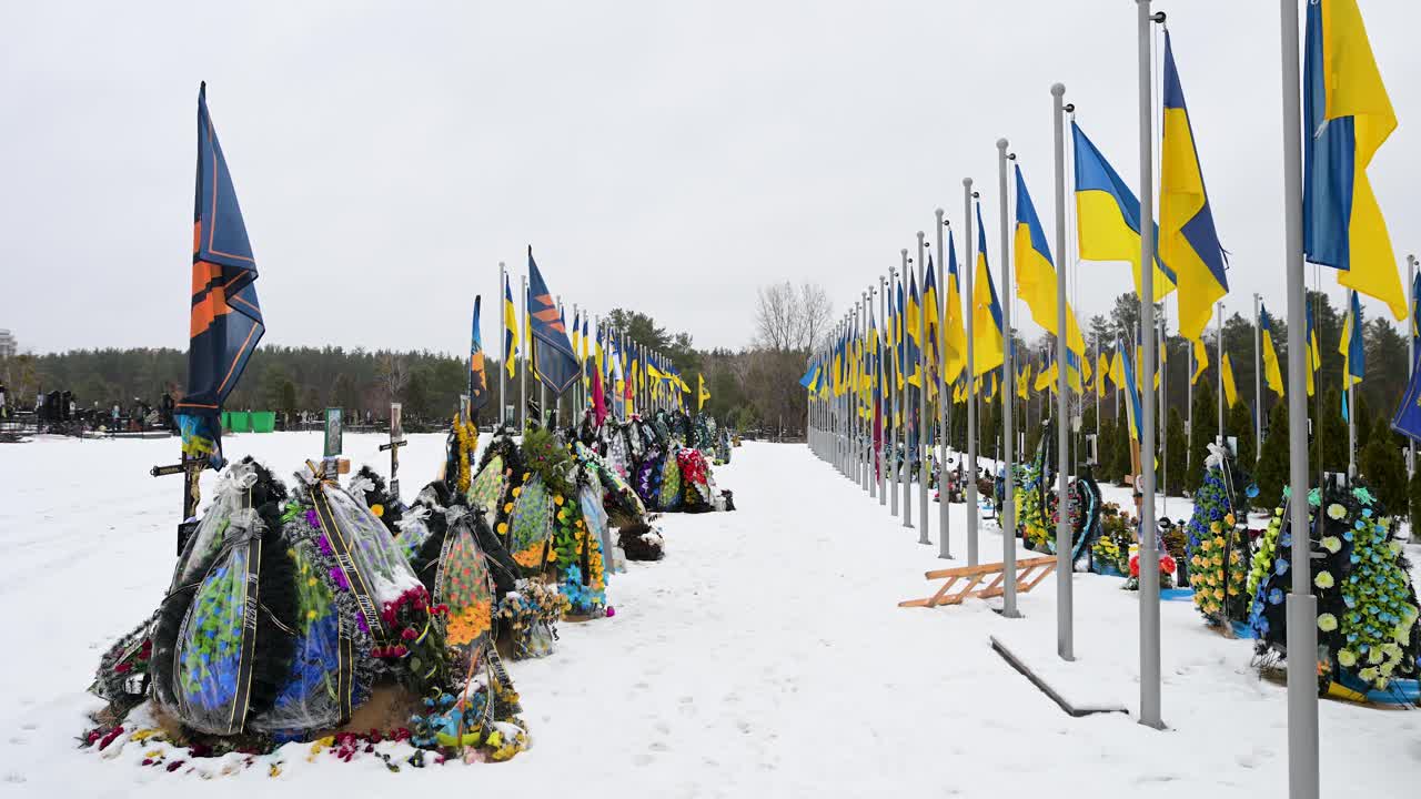 Snow-covered Irpin cemetery in Ukraine, where national flags stand tall in the wind above the graves of fallen Ukrainian soldiers from the Ukraine-Russia war.