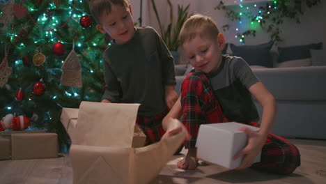 two boys unpack christmas presents under a christmas tree. children open gifts. high quality 4k footage