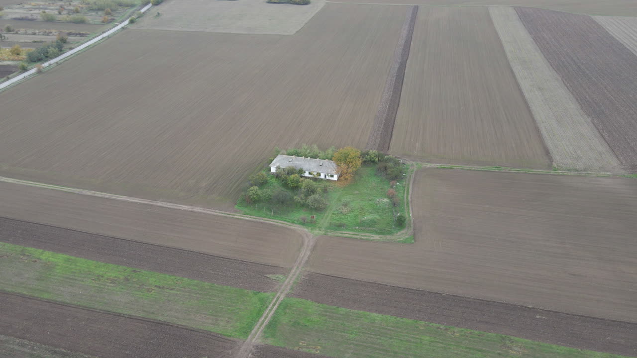 Drone luftbillede kredser over et smukt hvidt bondehus på en brun eng i landlige omgivelser.