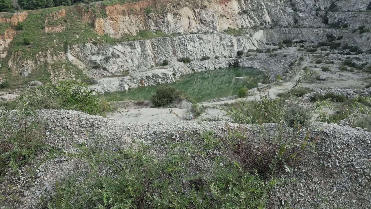 Green water gradually pooling inside abandoned quarry, transforming desolate rocky landscape into emerging small lake through natural accumulation process