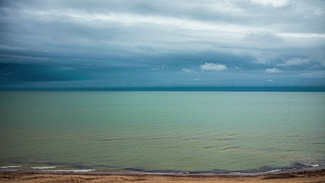 toma de lapso de tiempo del movimiento de la nube oscura sobre la orilla del mar con las olas estrellándose a lo largo de un día lluvioso