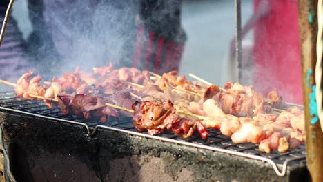 person turning skewers on a smoky barbecue grill