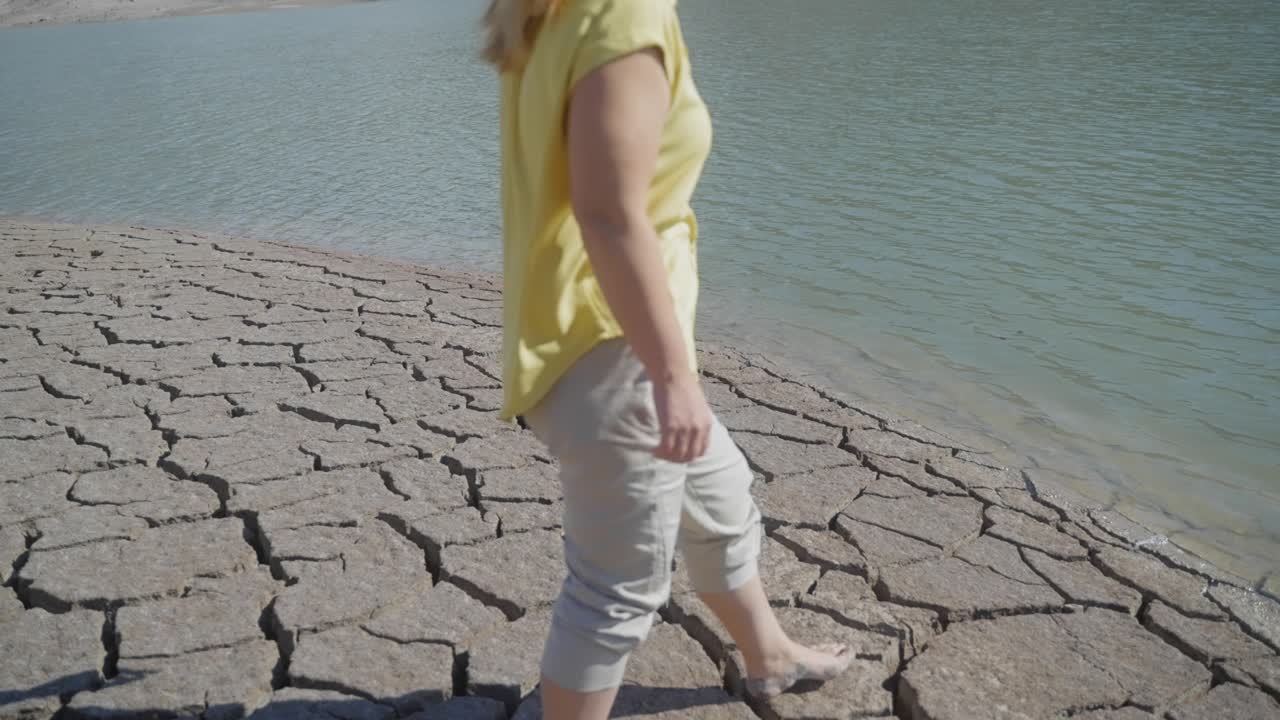 건조하고 갈라진 사막 풍경을 가로질러 걸어간 후 물에 접근하는 소녀의 중간 샷