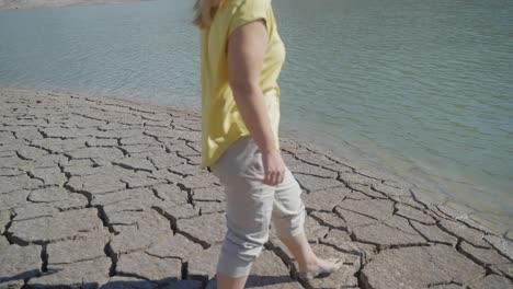 medium shot of a girl approaching water after walking across a dry, cracked desert landscape